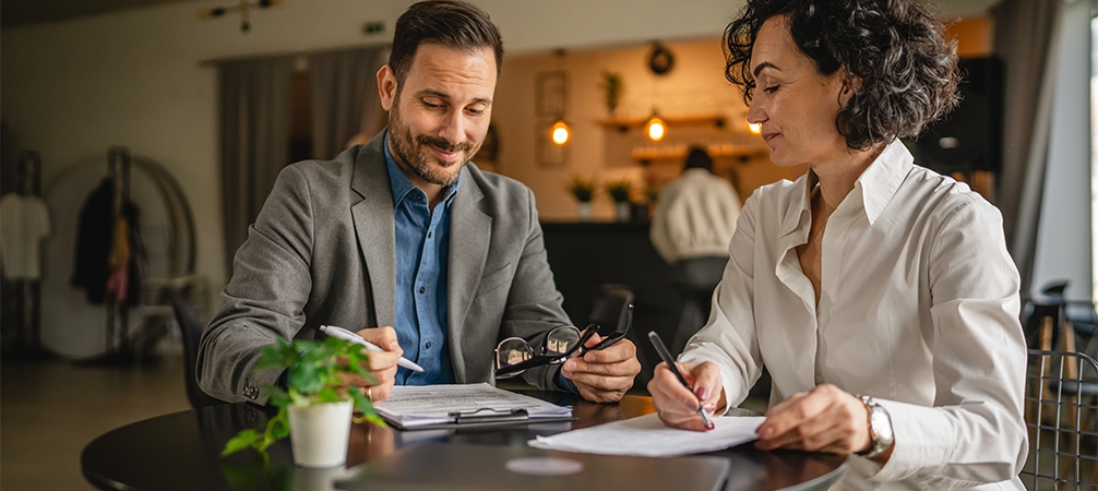 Two business professionals reviewing and signing insurance documents at a table.